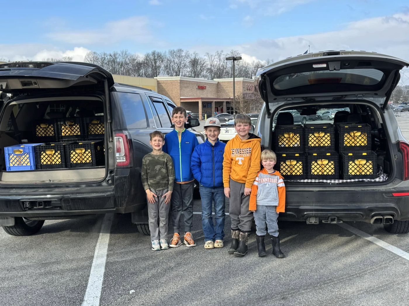 Five kids standing between two SUVs loaded with milk crates