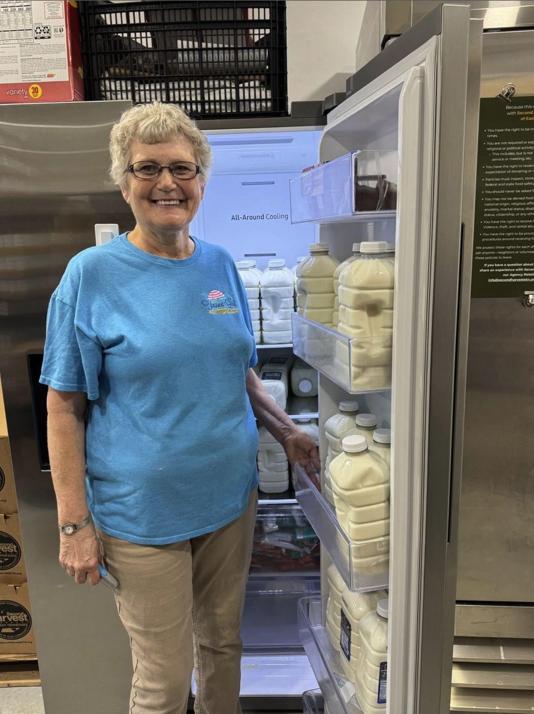A pantry volunteer beside a refrigerator stocked with milk