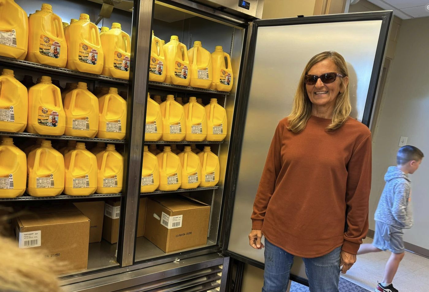 A volunteer next to a pantry fridge full of gallons of milk