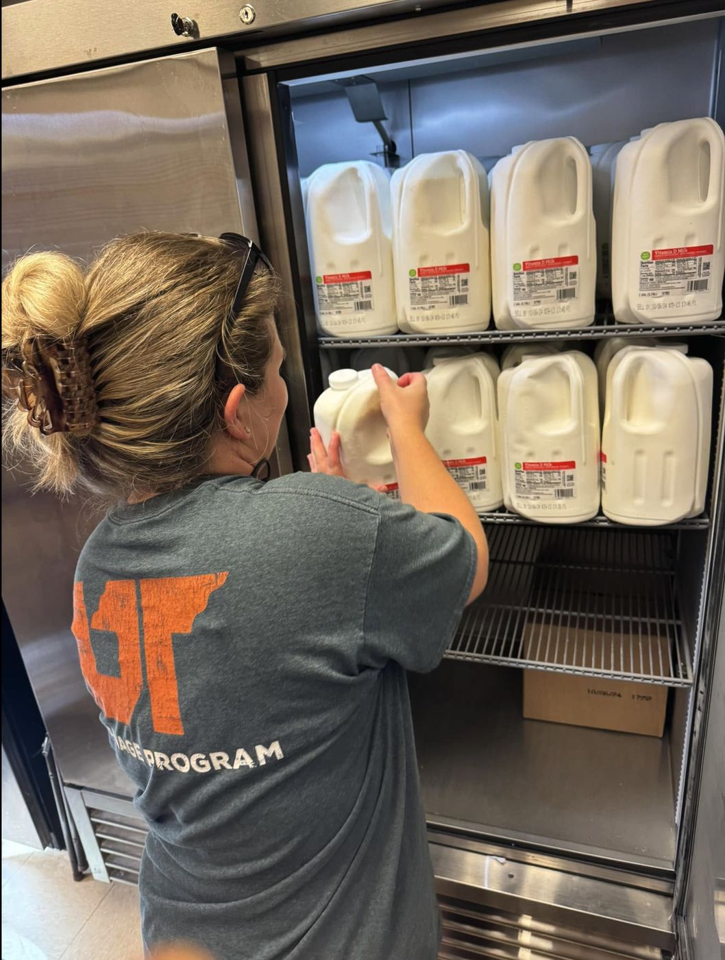 A volunteer stocking a pantry fridge with gallons of milk